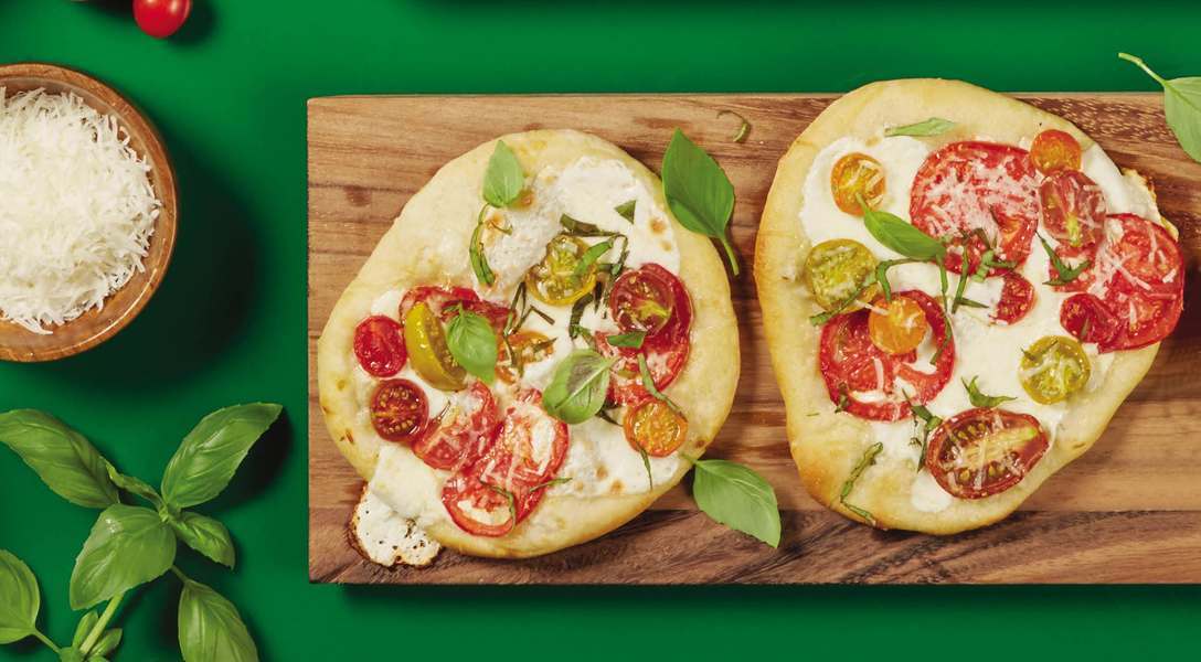 Two small pizzas topped with tomato and basil