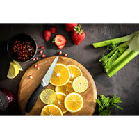 Image shows small paring knife with sliced lemons on a chopping board. There are strawberries and celery nearby.